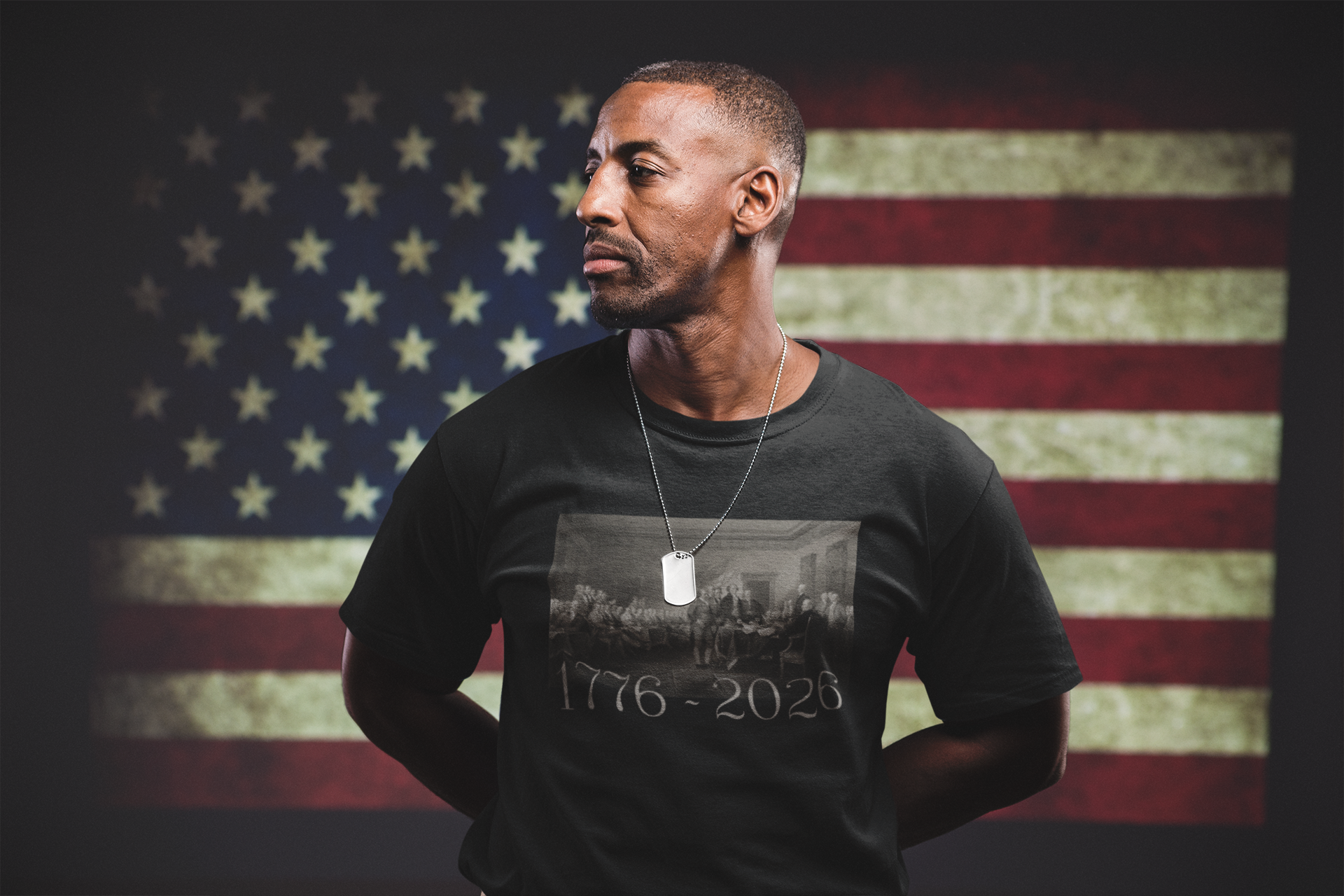 Soldier standing in front of a flag wearing America 250 Declaration of Independence t-shirt, featuring John Trumbull’s masterpiece in warm sepia tones, with 1776-2026 in Revolutionary era lettering