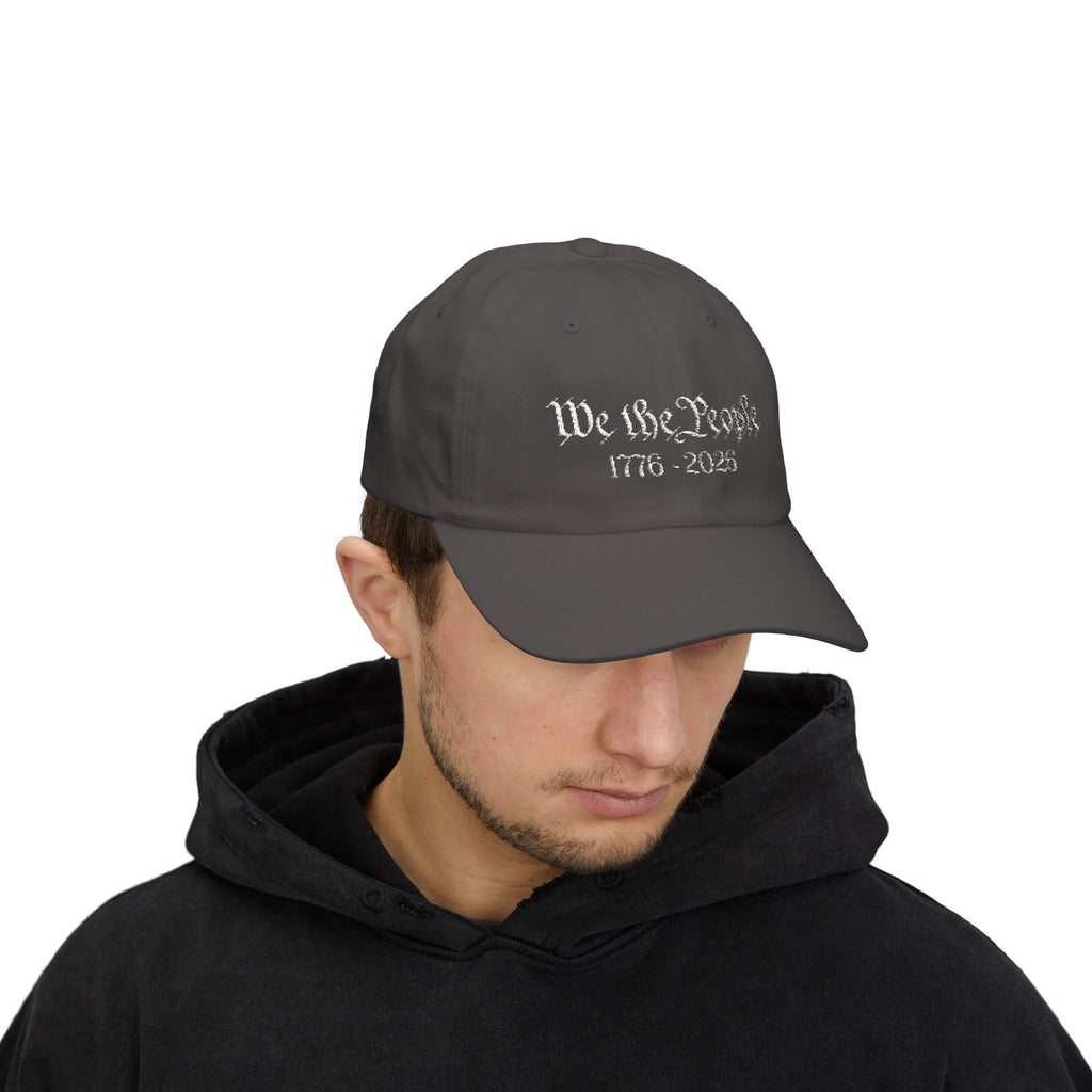 Man wearing a dark grey cap embroidered with "We the People 1776-2026"
