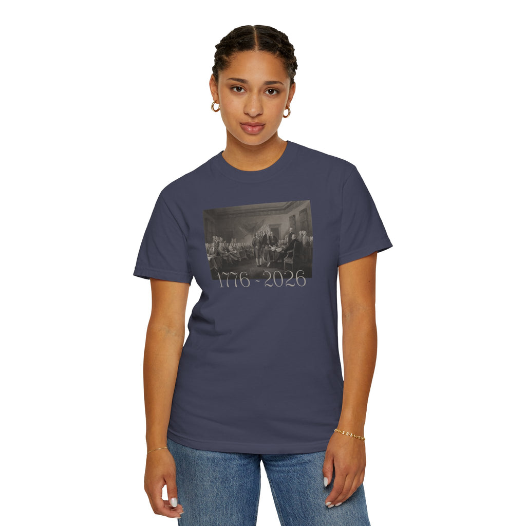 Woman wearing a Denim Comfort Colors t-shirt with a printed design of Trumbull's  'Declaration of Independence' painting with '1776-2026' in overlapping revolutionary era text