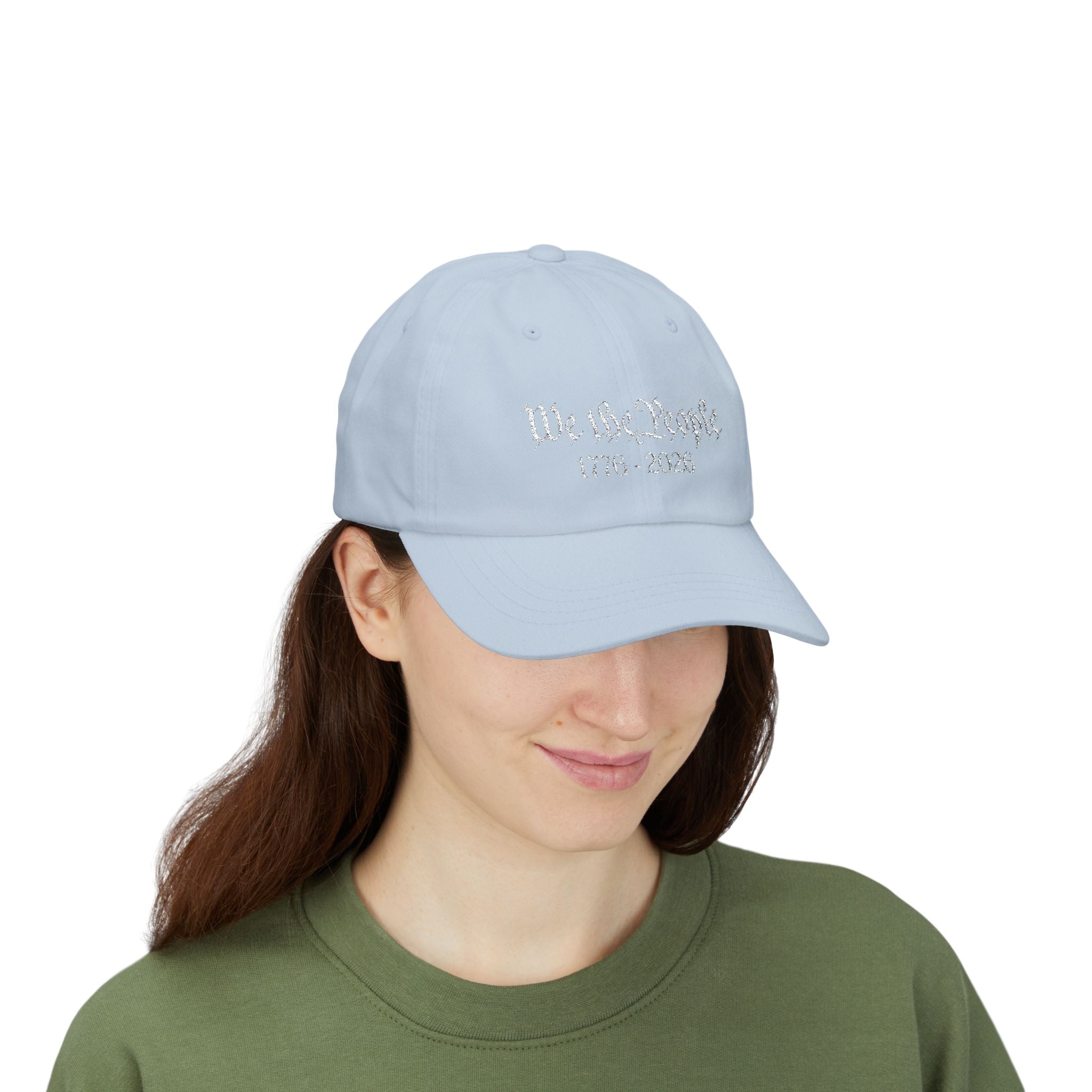Woman wearing a light blue cap with embroidered "We the People 1776-2026" 