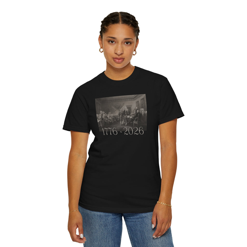 Woman wearing a Black Comfort Colors t-shirt with a printed design of Trumbull's  'Declaration of Independence' painting with '1776-2026' in overlapping revolutionary era text