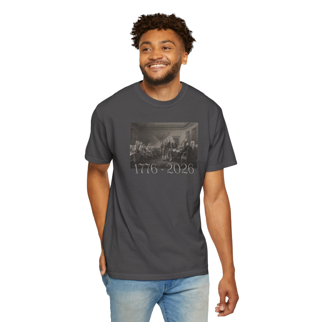 Smiling man wearing a Graphite Comfort Colors t-shirt with a printed design of Trumbull's  'Declaration of Independence' painting with '1776-2026' in overlapping revolutionary era text