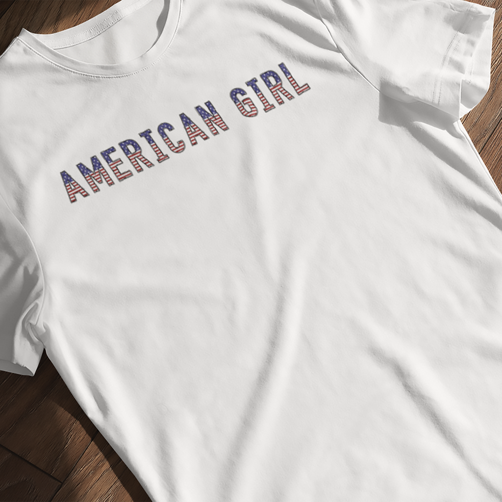 'American Girl' patriotic t-shirt with stars and stripes lettering laying flat on a wooden surface
