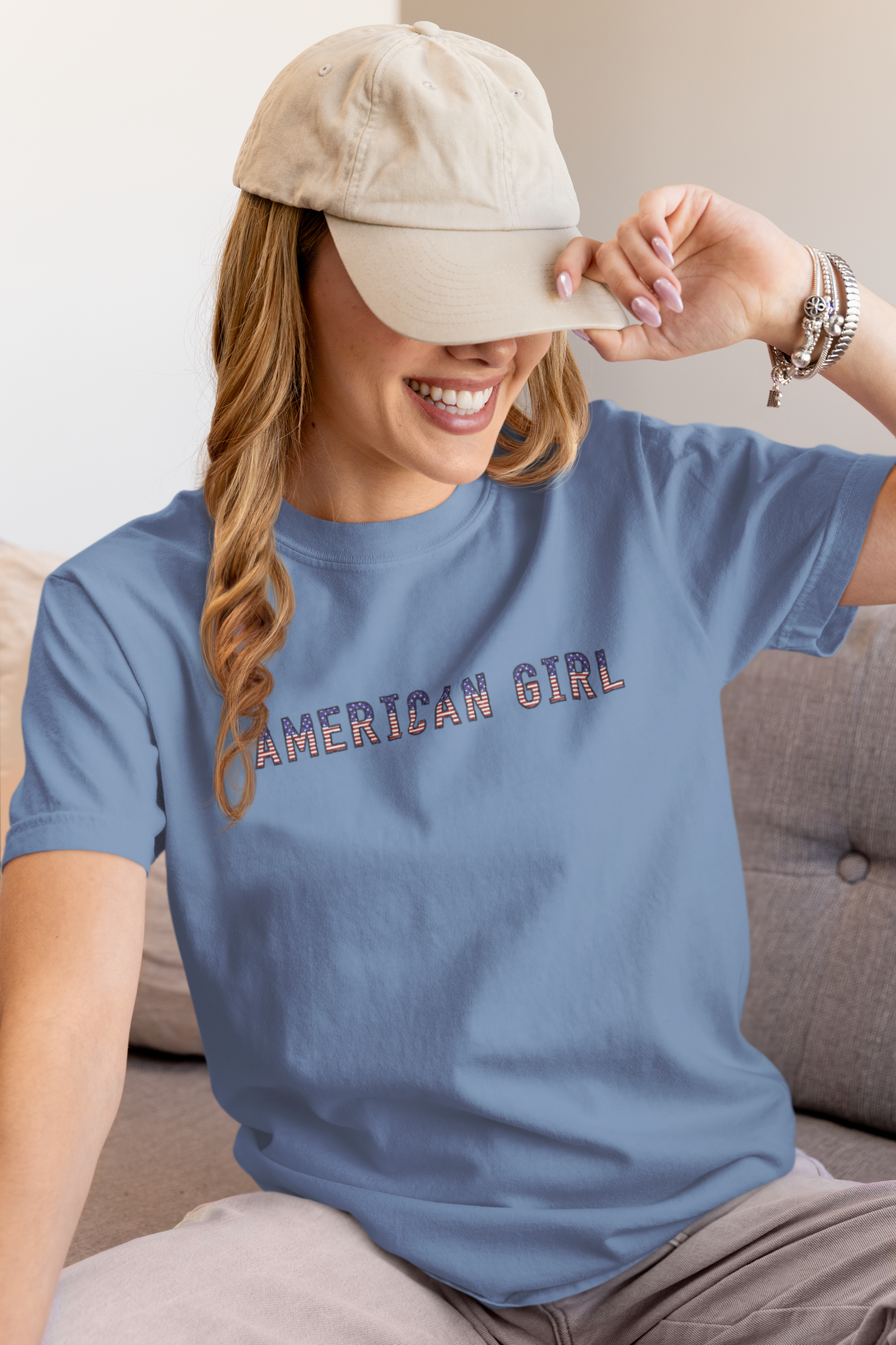Woman wearing a washed denim t-shirt with 'American Girl' in patriotic stars & stripes text, sitting on a couch.