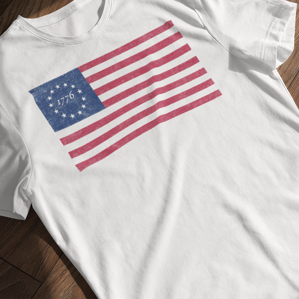 Distressed Betsy Ross flag 1776 t-shirt laying on a wooden surface

