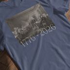 Denim Comfort Colors t-shirt with a printed design of Trumbull's  'Declaration of Independence' painting with '1776-2026' in overlapping revolutionary era text laying flat against a wooden background