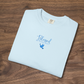 'Blessed Are the Peacemakers' Christian t-shirt embroidered with cornflower blue thread, folded, laying on a wooden surface
