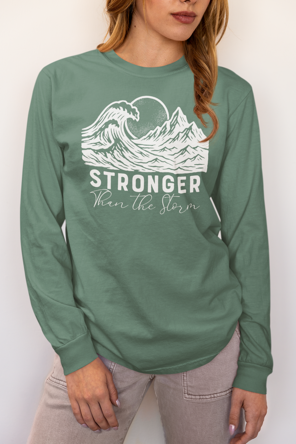 Woman wearing Stronger Than The Storm long sleeve faith t-shirt in light green