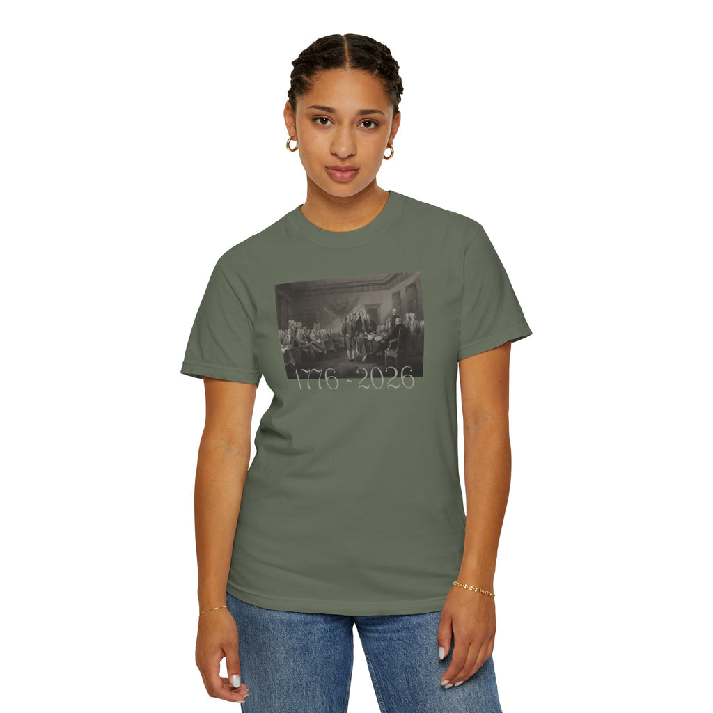 Woman wearing a Moss Comfort Colors t-shirt with a printed design of Trumbull's  'Declaration of Independence' painting with '1776-2026' in overlapping revolutionary era text