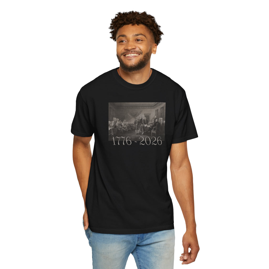 Smiling man wearing a Black Comfort Colors t-shirt with a printed design of Trumbull's  'Declaration of Independence' painting with '1776-2026' in overlapping revolutionary era text