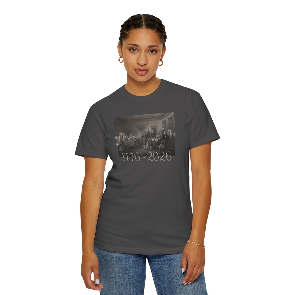 Woman wearing a Graphite Comfort Colors t-shirt with a printed design of Trumbull's  'Declaration of Independence' painting with '1776-2026' in overlapping revolutionary era text