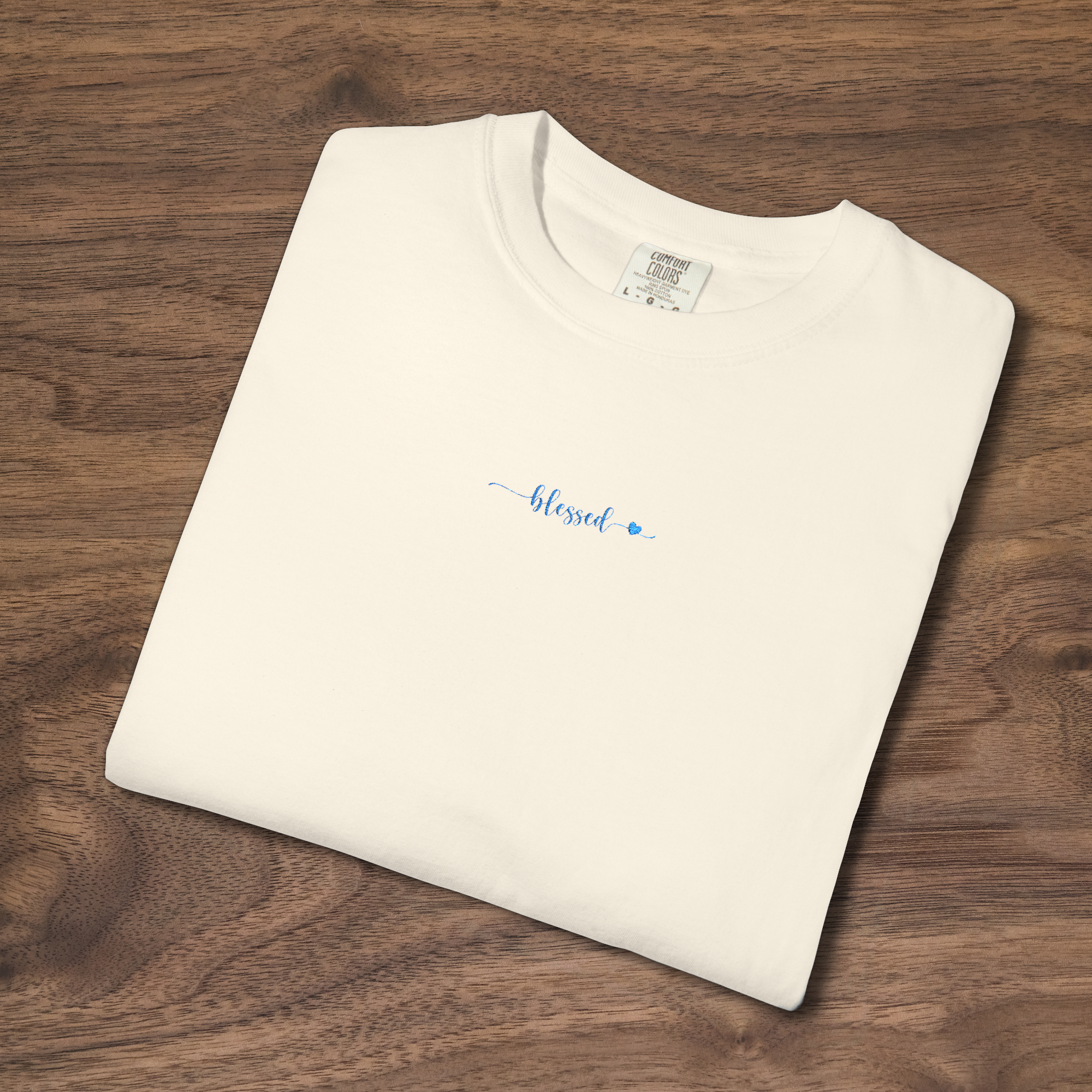 'Blessed' Christian t-shirt embroidered with cornflower blue thread, folded, laying on a wooden surface